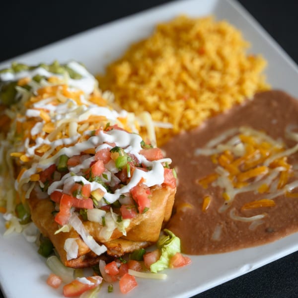 Two chimichangas topped with pico de gallo, sour cream, and cheese, served with rice and refried beans.