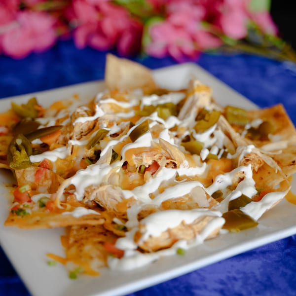 Chicken nachos with melted cheese, jalapeños, pico de gallo, and sour cream on a white plate.