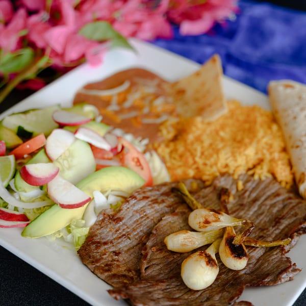 A Mexican dish with grilled steak, rice, beans, salad, and tortillas on a white plate.