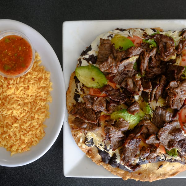 Papa Joe's Mexican Restaurant's carne asada tostada with rice and salsa on a dark table.